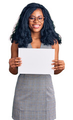 Beautiful african american woman holding blank empty banner looking positive and happy standing and smiling with a confident smile showing teeth