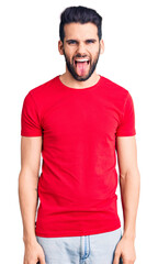 Obraz premium Young handsome man with beard wearing casual t-shirt sticking tongue out happy with funny expression. emotion concept.