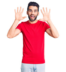 Young handsome man with beard wearing casual t-shirt showing and pointing up with fingers number ten while smiling confident and happy.