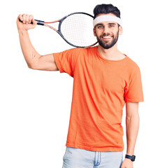 Young handsome man with beard playing tennis holding racket looking positive and happy standing and smiling with a confident smile showing teeth