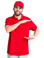 Young handsome man with beard wearing delivery uniform gesturing with hands showing big and large size sign, measure symbol. smiling looking at the camera. measuring concept.