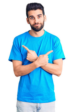 Young handsome man with beard wearing casual t-shirt pointing to both sides with fingers, different direction disagree