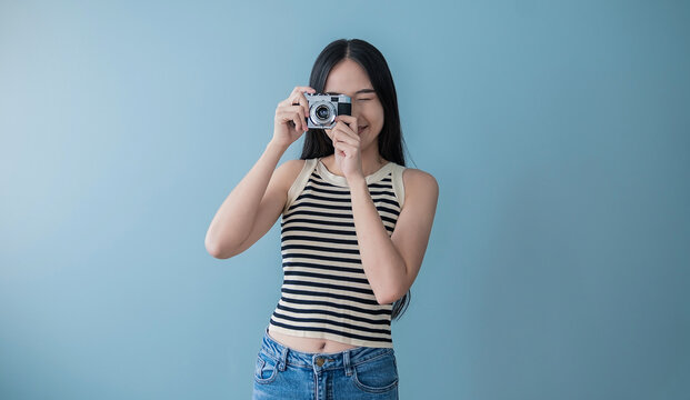Portrait of beautiful asian woman photographer in fashion look taking photo. Pretty cool young woman model with camera isolated on blue background with copy space banner. Asian travel lady girl.