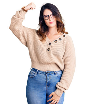 Beautiful young brunette woman wearing casual clothes and glasses strong person showing arm muscle, confident and proud of power