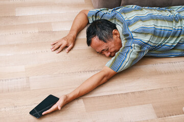Unconscious old man lying on floor with epileptic seizures at home while holding mobile phone.