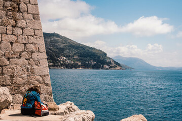 mujer sentada en el borde de piedra mirando al mar