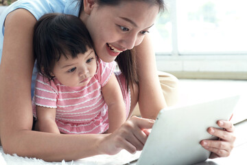 Fototapeta premium Young mother and baby girl pay attention to the pictures displayed on the tablet computer screen