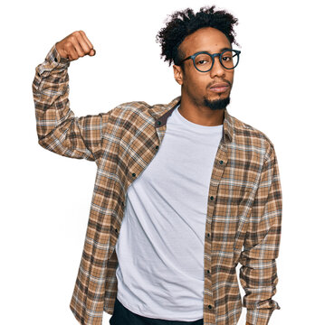 Young african american man with beard wearing casual clothes and glasses strong person showing arm muscle, confident and proud of power