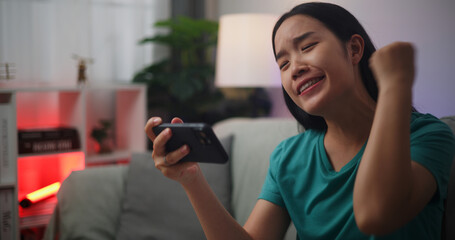 Portrait of Young Asian woman enjoys playing online esport games on smartphone sitting on sofa in...