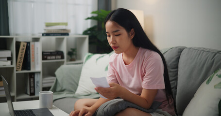 Portrait of Young Asian woman holding paper various expense bills and plans for personal finances and using calculator on smartphone calculate Income and expenses at home,Home finance