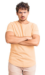 Young handsome man with curly hair wearing casual clothes skeptic and nervous, disapproving expression on face with crossed arms. negative person.