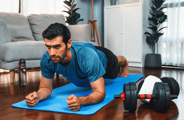 Athletic and sporty man doing plank on fitness mat during home body workout exercise session for...