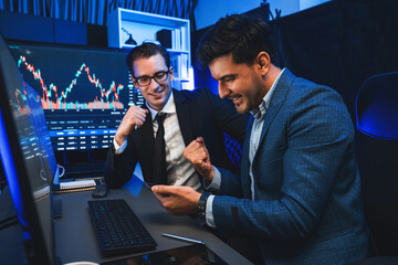 Two stock exchange traders comparing dynamic investment graph via phone and pc with high profit in...