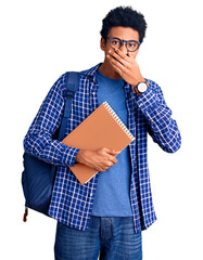Young african american man wearing student backpack holding book laughing and embarrassed giggle covering mouth with hands, gossip and scandal concept