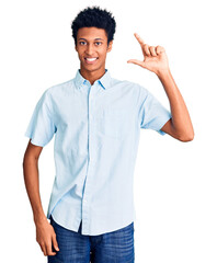 Young african american man wearing casual clothes smiling and confident gesturing with hand doing small size sign with fingers looking and the camera. measure concept.