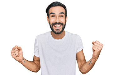 Young hispanic man wearing casual white t shirt celebrating surprised and amazed for success with arms raised and open eyes. winner concept.