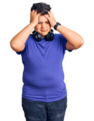 Little boy kid listening to music wearing headphones suffering from headache desperate and stressed because pain and migraine. hands on head.