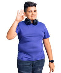 Fototapeta premium Little boy kid listening to music wearing headphones smiling positive doing ok sign with hand and fingers. successful expression.
