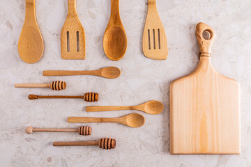 A set of various wooden spoons, spatulas, cutting board made of eco-friendly materials on a light stone countertop. kitchen background. Top view.
