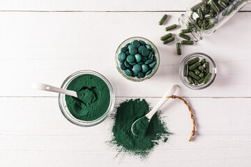 Round blue-green natural spirulina algae tablets and powder in bowl on white background. medical...