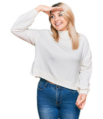 Fototapeta premium Young caucasian woman wearing casual winter sweater very happy and smiling looking far away with hand over head. searching concept.