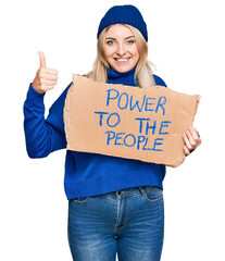 Young caucasian woman holding power to the people banner smiling happy and positive, thumb up doing excellent and approval sign