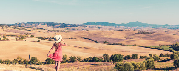 Holiday in Tuscany- Young female tourist in red dress and hat enjoying panoramic Tuscan landscape...