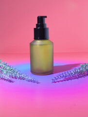 A Mock Up of a Yellow Green Beauty Cosmetic Bottle Packaging with Purple Lavender Sprigs on an Orange, Pink and Purple Dreamy Gradient Background