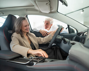 Fototapeta na wymiar An elderly couple chooses a new car at a car dealership. Mature woman driving. 
