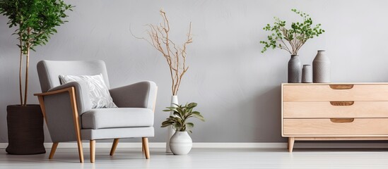 Trendy Scandinavian living room with wooden commode, design armchair, carpet, leaf in vase, book, and personal accessories in unique home decor.