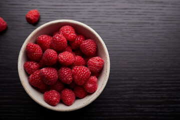 Top view of raspberries in a bowl on wood table background.