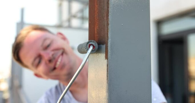 Positive male houseworker paints new railings on balcony