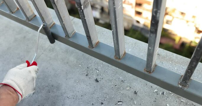 Male houseworker in gloves paints new railings on balcony