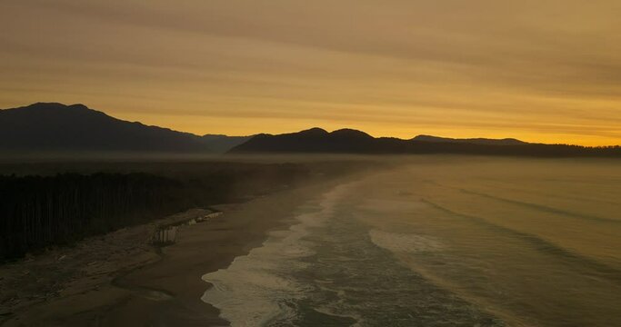 Stunning golden sunset above Bruce Bay with waves hitting shore, aerial