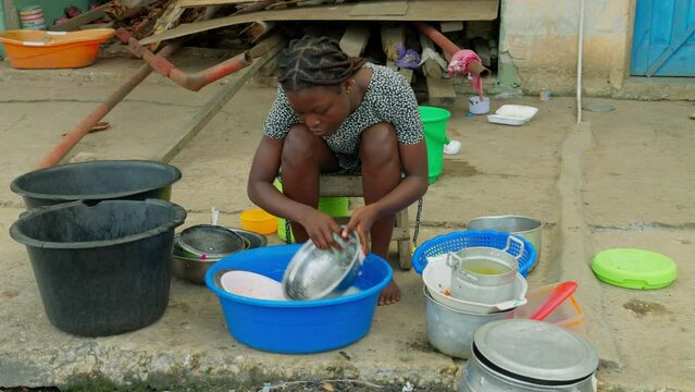 Making sure that her kitchen utensils are clean, a local woman is washing dishes in front of her house in a village in Kumasi, Ghana, Africa.