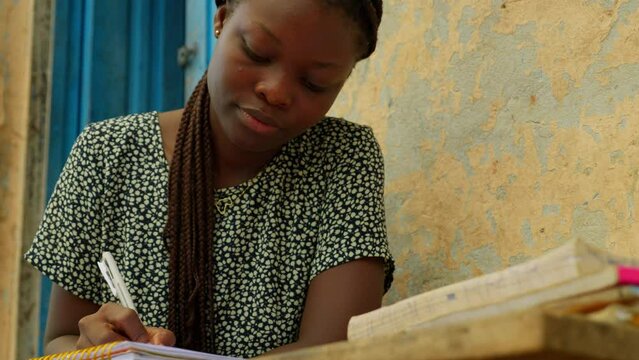 Taking some notes from a book while studying, a young woman is educating herself to bridge the gender gaps in Kumasi, Ghana, Africa.