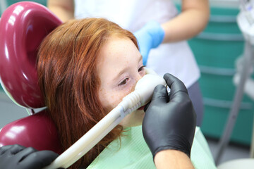 A little girl is injected with an inhalation sedative during dental treatment at a dental clinic. Dental treatment for a child. Anesthesia for children in dental treatment.