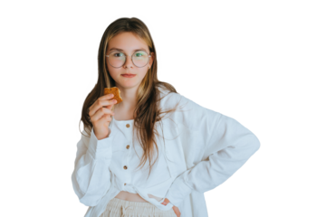 Teen girl in glasses and white shirt eats cookie looks at camera against transparent background. Brunette American girl at morning preparing for school feeding. Domestic leisure. Teenagers
