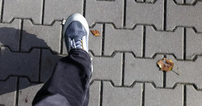 Human feet in sneakers walk along dark sidewalk in town