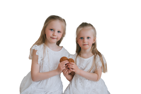 Two blonde Swedish sisters sitting against transparent background holding cookies. Little American girls in white dresses making heart shape with cookies. Childhood, sweets, bakery. - Powered by Adobe