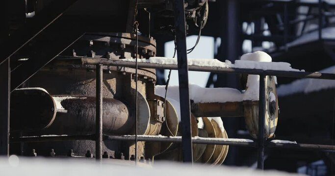 Close-up of rusted machinery that is part of a larger structure consisting of pipes, valves and tanks. All covered in snow and abandoned.