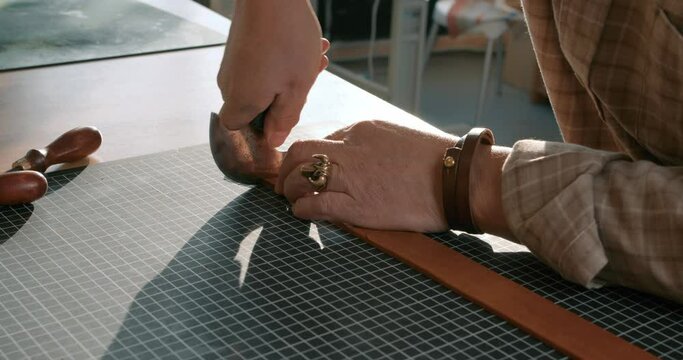 old man's hands making hole in new leather belt, handmade products, accessories Slow motion Tailor working with a hammer