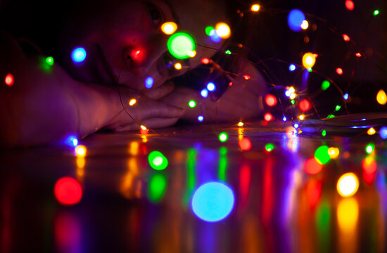 Fototapeta Woman in dark looks colorful lights of New Year garland....