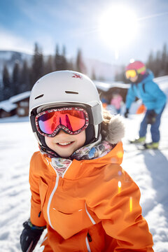 A cheerfully smiling child in a ski suit, helmet and ski goggles on a snow-covered slope.