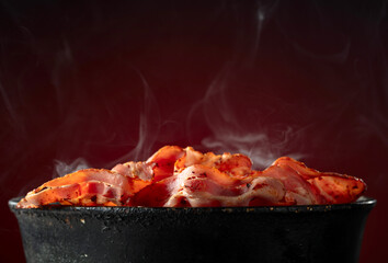Fried steaming bacon slices in an old black pan.