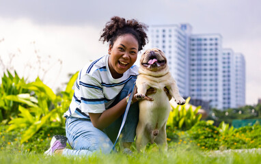 African American woman is playing with her french bulldog puppy while lying down in the grass lawn after having morning exercise in the public park