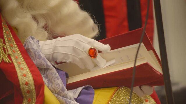 Hand of Saint Nicholas with white glove and ruby ring leafing through holy red book