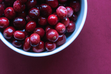 Overhead shot of cranberries in white bowl on red surface.