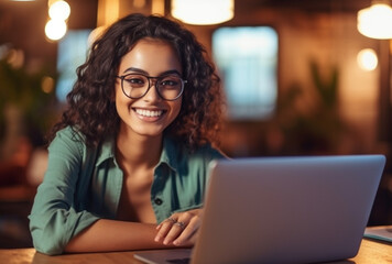 Attractive young indian woman sitting in front of a laptop smiling