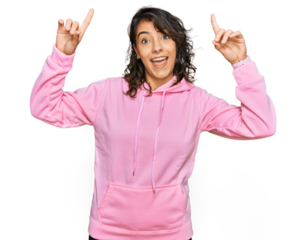 Young hispanic woman wearing casual sweatshirt smiling amazed and surprised and pointing up with fingers and raised arms.